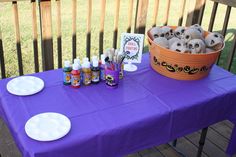 a purple table topped with lots of bottles and plates filled with stuff sitting on top of a wooden deck