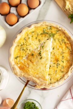 a quiche being held up by a spatula in front of eggs and other ingredients