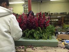 a man in a white jacket is working on some red and green plants at a flower shop