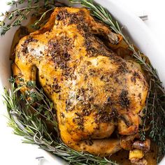 a close up of a chicken in a bowl with herbs on the side and seasoning