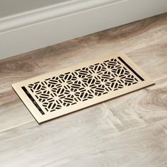 a floor grate with an intricate design on the top and bottom, in front of a white wall