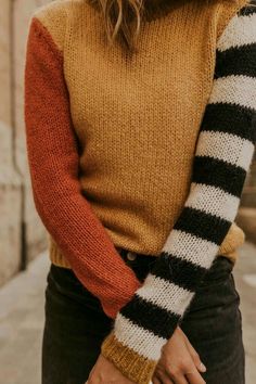 a woman wearing an orange and black sweater with stripes on the sleeves is standing in front of a stone building