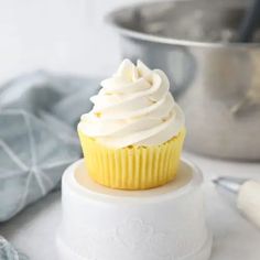 a cupcake sitting on top of a white cake plate next to a metal pan