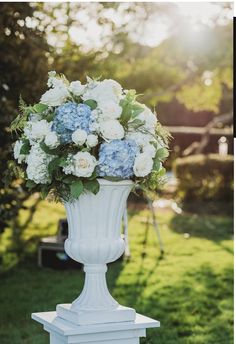 a white vase filled with blue and white flowers sitting on top of a lush green field