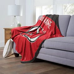 a couch with a red and black blanket on top of it next to a lamp