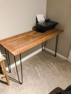 a wooden table with hairpin legs and a printer on it in the corner of a room