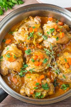 chicken stew with carrots and parsley in a silver pot on a wooden table