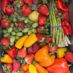 there are many different fruits and vegetables in the bin together, including strawberries, asparagus, lemons, tomatoes, peppers, cucumbers, broccoli, and more