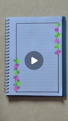 an open spiral notebook with pink flowers and green vines on the side, next to a video play button