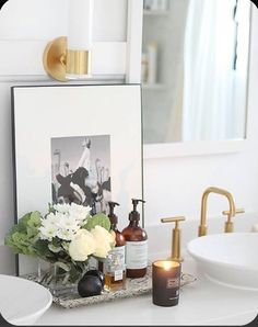 a white sink sitting under a bathroom mirror next to a vase with flowers on it