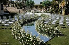 an outdoor ceremony setup with chairs and flowers on the grass, in front of palm trees