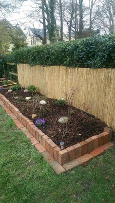 a garden with brick edgings and plants in the ground next to a fence