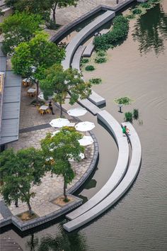 people are sitting at tables on the edge of a large body of water with umbrellas over them