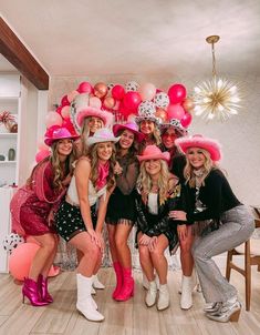 a group of women in pink hats posing for a photo with balloons on the wall behind them