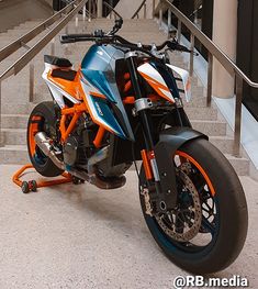 an orange and black motorcycle parked on the street next to some stairs with handrails