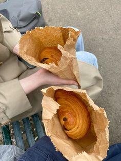 two people sitting on a bench holding up some food in their hands and looking down at the ground