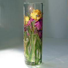 a glass vase with purple and yellow flowers on the inside is sitting on a white surface