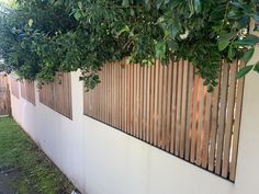 a white wall with wooden slats on it and grass in the foreground, next to a tree