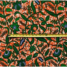 an orange and green floral print fabric with white dots on the bottom, in front of a ruler