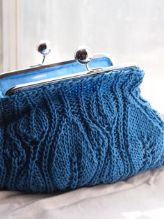 a blue purse sitting on top of a white bed next to a window sill