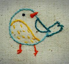 a small embroidered bird sitting on top of a piece of cloth