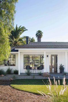 a small white house with palm trees in the back ground and grass on the front lawn