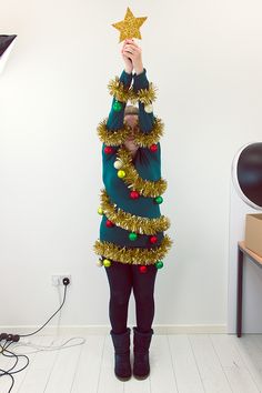 a woman standing in front of a white wall holding up a star shaped christmas tree