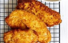 three fried chicken patties on a cooling rack next to a bowl of dipping sauce