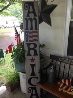 an american flag sign on the side of a house with flowers and potted plants