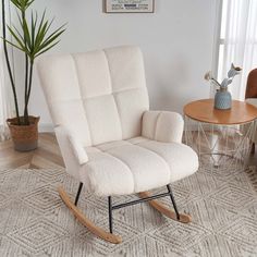 a white rocking chair sitting on top of a rug next to a potted plant