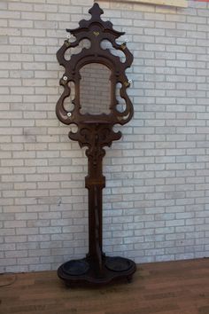 an ornate wooden mirror stands against a white brick wall in front of a wood floor