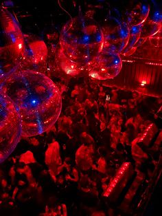 many people are gathered around disco balls in red and blue lights at a club or nightclub