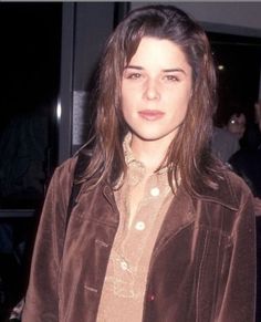 a woman standing in front of a crowd wearing a brown jacket