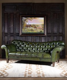 a green leather couch in front of a wooden paneled wall with a painting on it