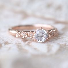 a rose gold engagement ring with three stones on top, sitting on a white blanket