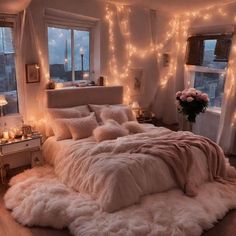 a bedroom with lights strung over the windows and a bed covered in fluffy pink blankets