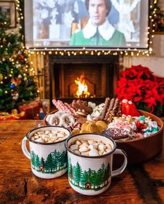 two mugs filled with hot chocolate and marshmallows in front of a fireplace