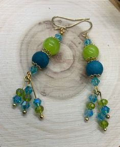 a pair of blue and green beaded earrings sitting on top of a piece of wood