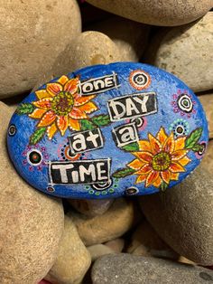 a painted rock that says one day at a time with sunflowers on it