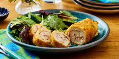 a blue bowl filled with meat and salad on top of a wooden table next to utensils