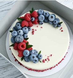 a cake decorated with berries and blueberries in a white box on a wooden table