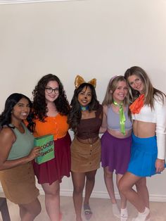 four girls dressed up in costumes posing for the camera with one girl holding a book