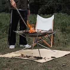 a man standing next to a chair on top of a grass covered field near a fire