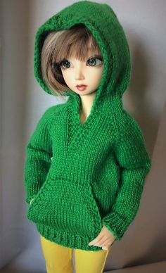 a doll is wearing a green sweater and yellow pants with her hands in her pockets