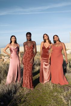 three women in long dresses standing next to each other on a hill near the ocean