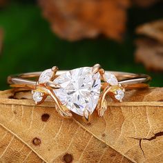 a heart shaped diamond ring sitting on top of a leaf