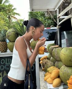 a woman standing in front of a fruit stand with lots of melons and pineapples