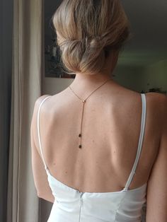 the back of a woman's white dress with a gold necklace on her neck