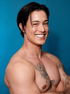 a shirtless man with tattoos on his chest posing for a photo in front of a blue background