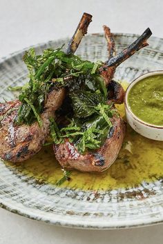 a plate topped with meat and greens next to a small bowl of dipping green sauce